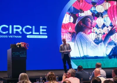 Speaker presenting on stage in front of a large CIRCLE 2025 screen with a vibrant cultural image.