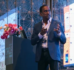 Man speaking at podium with flowers and geometric background at CIRCLE 2025 event.