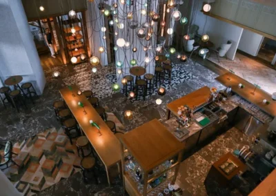 Overhead view of a modern café or lounge with wooden tables, bar counter, eclectic pendant lighting, and patterned flooring