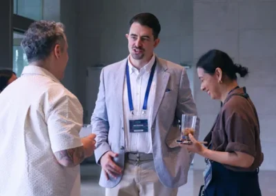 Three conference attendees chatting casually, with name badges around their necks, in a modern indoor venue.