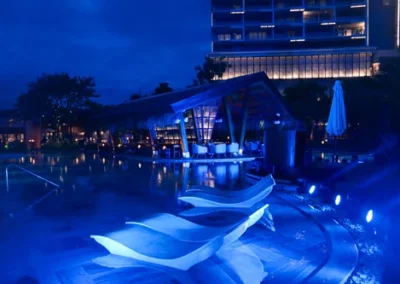 Poolside lounge chairs and illuminated bar area at a luxury resort at night, bathed in blue lighting.