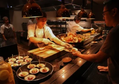 Chef serving freshly prepared food to a guest at a buffet station under warm lighting, with various gourmet dishes displayed.