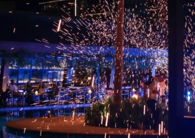 Sparks fly through the air during a nighttime fire performance by the poolside at a luxury resort.